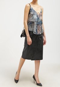 Blusa de capas multicolorida con escote en V profundo, con un patrón en azul y beige, combinada con una falda lápiz de cuero negro y tacones altos.