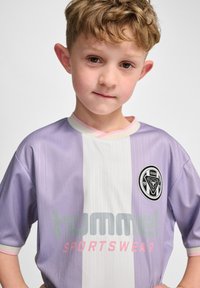 Koszulka piłkarska w kolorze lawendowym i białym w paski, z krótkim rękawem, z okrągłym logo, kontrastowym kołnierzykiem oraz napisem "hummel SPORTSWEAR" pod logo.