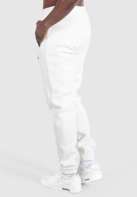 Weiße Jogginghosen aus einem weichen, strukturierten Stoff, mit elastischem Bund und seitlichen Taschen, kombiniert mit weißen Turnschuhen. Einfaches Design mit bequemer Passform.