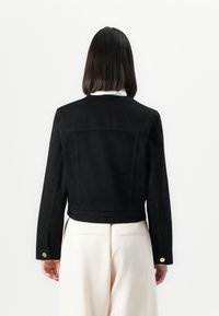 Veste en denim noir au design court, avec un dos uni, des manches longues et des accents de boutons dorés sur les poignets.