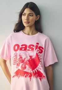 Roosa puuvillane T-särk, millel on erksad punased graafikad, sealhulgas "Oasis" tekst, albumi kaanepilt ja "Definitely Maybe" tekst allosas.