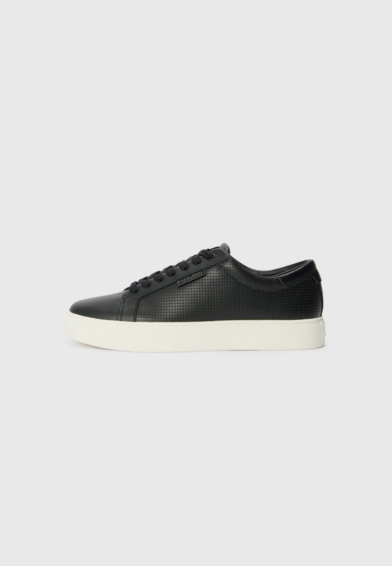 Sneakers de couro preto com textura perfurada, bico redondo e sola de borracha branca plana. Apresenta atacadores pretos e um logótipo discreto na lateral.