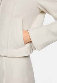 White wool-blend jacket with a textured finish, featuring a straight-cut silhouette, side pockets, and a clean, minimalist design.