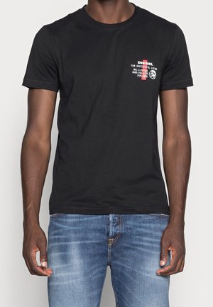 T-shirt en coton noir à manches courtes, avec un imprimé graphique rouge et blanc sur la partie gauche de la poitrine. Coupe ajustée avec col rond.