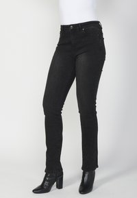 Vaqueros skinny de mezclilla negra con una cintura de altura media, que presentan sutiles acentos de tachuelas y un diseño clásico de cinco bolsillos. Combínalos con botas de tacón negro.