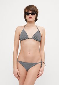 Svart-hvitt stripete bikini med trekantet topp og knytbare bukser. Materialet ser glatt og lett ut. Modellen har på seg solbriller.