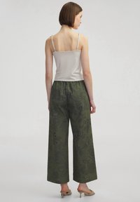 Pantalones de pierna ancha en verde oliva con detalles de bordado floral, combinados con una camiseta sin mangas beige. Textura suave, corte holgado y sutiles adornos.