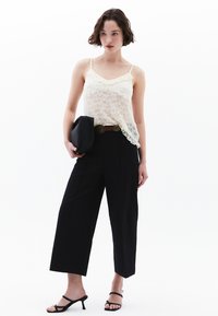 Krämfärgad topp med spetsdetaljer, svarta vida byxor, svart clutchväska, och svarta sandaler med remmar. Texturerat tyg och lös passform.