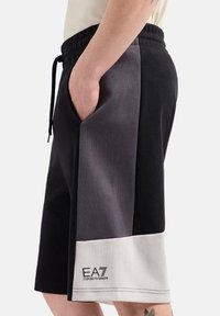Shorts sportivi neri e grigi con elastico in vita, tasche laterali e un'etichetta logo bianca sull'orlo, caratterizzati da un design a blocchi di colore.