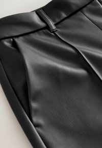 Zwarte nep leren broek met een gladde textuur, geplooid ontwerp en een dunne tailleband met een subtiel sluitingsdetail.