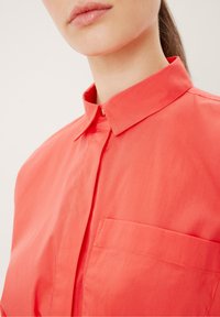 Camicia button-up corallo con colletto e taschino sul petto; presenta un tessuto morbido e leggero e una vestibilità su misura.
