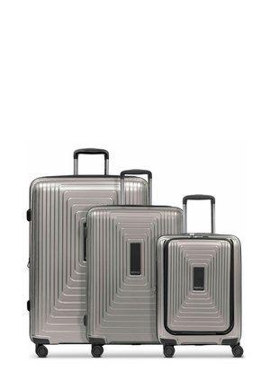 Trois valises rigides emboîtées en argent, présentant un design à nervures texturées, rehaussées de poignées et de roues noires.