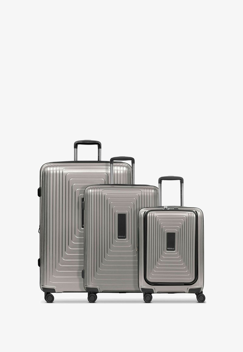 Tre valigie rigide sovrapposte in argento, con un design a coste testurizzate, accentuate da maniglie e ruote nere.