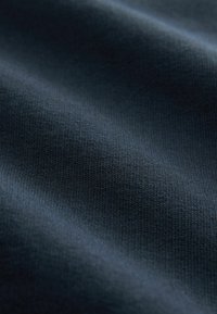 Zbliżenie na ciemnoniebieską tkaninę o delikatnej fakturze dzianiny i miękkich fałdach.