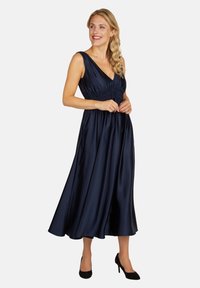 Robe en satin bleu marine avec un décolleté en V, une taille froncée et une jupe évasée fluide. Présente des bretelles larges et des poches latérales. Texture élégante et lisse.