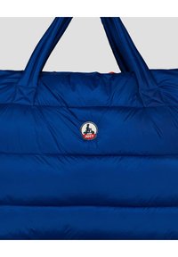 Sac rembourré bleu avec deux poignées et un logo circulaire présentant une silhouette sur un scooter au-dessus du texte rouge "JOTT".