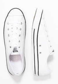 Hvide kanvas sneakers med sorte gummi detaljer, der har metaløjer, hvide snørebånd og en gummisål med et tekstureret mønster.