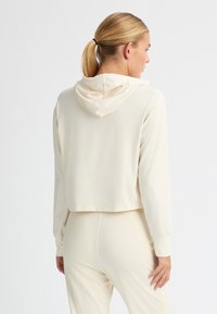 Hoodie accorciato in beige chiaro, realizzato in un tessuto morbido, con maniche lunghe e cappuccio. Design minimalista senza motivi o accenti visibili.
