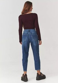 Ciemnofioletowa bluzka z długim rękawem w połączeniu z niebieskimi dżinsami o wysokim stanie. Dżinsy mają luźny krój, dwie tylne kieszenie i delikatne zwężenie. Czarne buty na platformie.