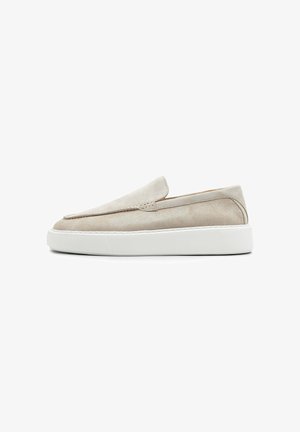 Beige suède instaploaier met witte dikke rubberen zool, afgeronde neus en minimale stiksel details, zijaanzicht op witte achtergrond.