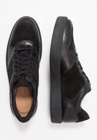 Czarne skórzane i zamszowe trampki o gładkim wykończeniu, zaokrąglonym nosku, zamykane na sznurówki, z grubą gumową podeszwą. Dyskretne logo widoczne.