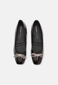 Ballerines en cuir verni noir avec un détail en noeud et des accents en ton argenté. Bout rond et semelles matelassées. Texture lisse.