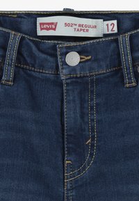 Jeans Levi's 502 Regular Taper en denim azul oscuro, con costuras amarillas, diseño tradicional de cinco bolsillos y cierre de botón metálico.