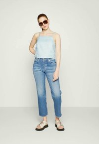 Top cropped de bolinhas azul claro, jeans azul desbotado de cintura alta e sandálias creme com design recortado, usadas com óculos de sol castanhos.