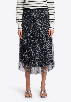 Mujer con falda midi plisada con estampado de cebra en negro y gris, top de manga larga a rayas y tacones plateados de punta abierta.