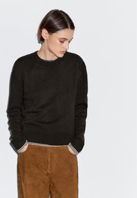 Donkerbruin gebreide trui met geribde manchetten en zoom, gecombineerd met tan suède broek met gestreepte zakdetails.