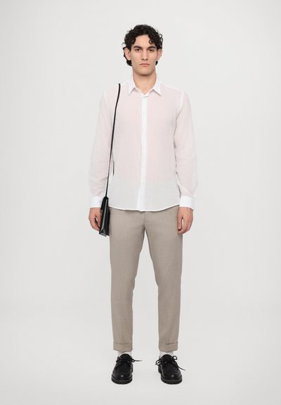 Camisa blanca de manga larga y botones; pantalones beige; zapatos negros; pequeña bolsa de crossbody negra; textura suave; paleta de colores neutros.