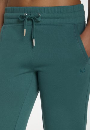 Türkise Baumwoll-Jogginghosen mit verstellbarem Kordelzugbund, Seitentaschen und subtiler Markenkennzeichnung. Der Stoff hat eine weiche, strukturierte Oberfläche.