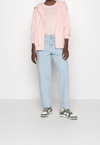 Růžová mikina na zip, světle růžové tričko, světle modré džíny se širokými nohavicemi a zelenobílé tenisky s černými tkaničkami. Měkká látka, volný střih.