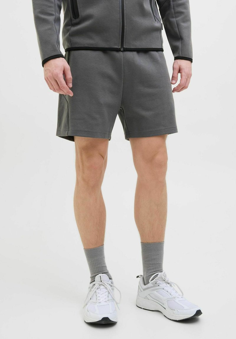 Grijze sportshorts van zacht materiaal, met een elastische tailleband en een comfortabele pasvorm, gedragen met witte sneakers en grijze sokken.