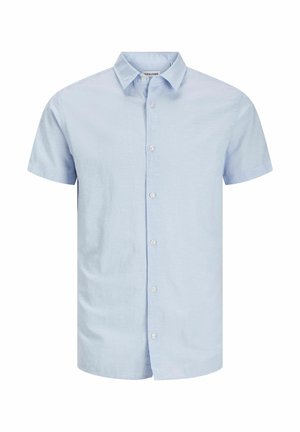 Enfant portant une chemise bleu clair à manches courtes boutonnée, un pantalon blanc ample et des chaussures noires à lacets sur fond blanc uni.