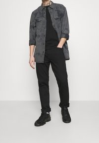 Svarta sneakers, svarta byxor och en gråfärgad skjorta med knappar och två bröstfickor. Skjortan är oversized med rullade ärmar.