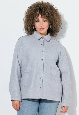 Harmaa fleece-takki, jossa on kauluskot, napit ja kaksi etutaskua. Pehmeä rakenne, rento istuvuus ja suora leikkaus.