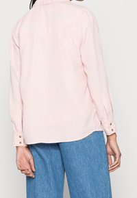 Lichtroze overhemd met knopen, lange mouwen, een western-stijl schouderstuk en twee knopen aan de manchetten, gemaakt van een glad, lichtgewicht stof.