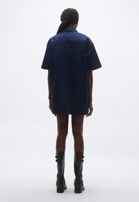 Tengerészkék, bő szabású ingruha sima anyagból, rövid ujjakkal és egyenes szabással, térdig érő fekete csizmával párosítva.