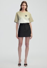 Top à manches courtes bicolore en beige et blanc, orné d'un embellissement en forme de cœur, associé à une mini-jupe noire élégante.