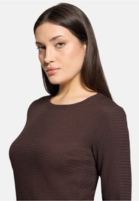 Braunes Langarmoberteil mit strukturiertem Muster, runden Ausschnitt und figurbetonter Silhouette, das seinen glatten Stoff und seine Form hervorhebt.