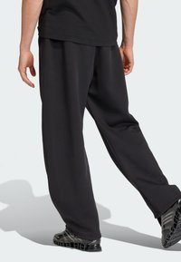 Černé sportovní kalhoty z měkké látky, s volným střihem a zúženými nohavicemi. Doplněné černou texturovanou obuví.
