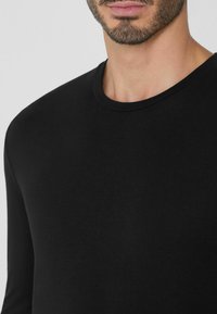 Schwarzes langärmliges Shirt aus glattem Stoff. Verfügt über einen klassischen Rundhalsausschnitt und eine taillierte Passform, mit minimalen Nähten und ohne Muster.