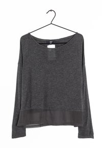 Langärmeliges, dunkelgraues Shirt mit einem Rundhalsausschnitt, strukturiertem Oberteil und einem transparenten unteren Saum. Hängt an einem schwarzen Drahthaken.