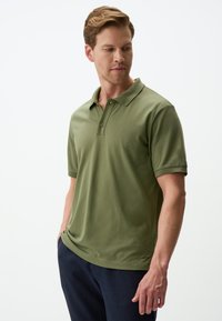 Polo shirt verde oliva realizzato in cotone morbido, con colletto, maniche corte e pattina con due bottoni. Vestibilità leggermente rilassata.