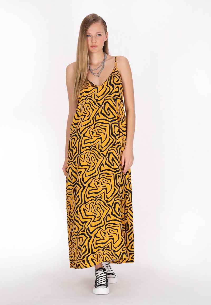 Rochie maxi galbenă cu un model abstract de spirale negre, cu bretele subțiri și o croială lejeră, asortată cu adidași negri și albi.