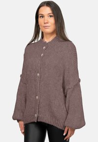 Cardigan ample en maille mauve avec de gros boutons, motif texturé, col montant et manches larges, associé à un pantalon noir ajusté.