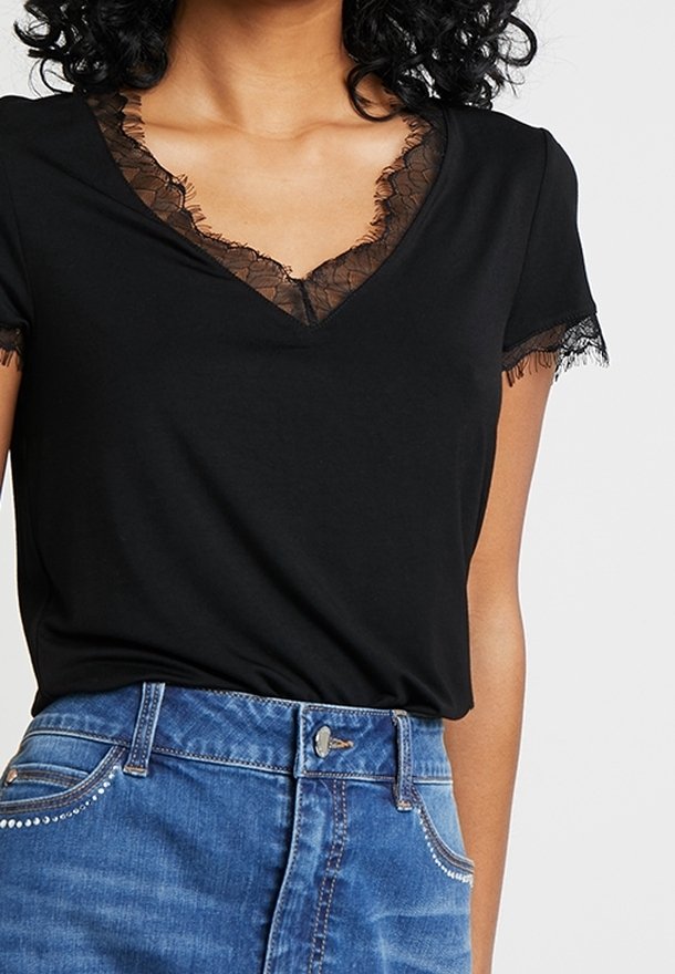 Camiseta negra de cuello en V con encaje alrededor del escote y las mangas, combinada con una falda de mezclilla azul clara con costuras decorativas.