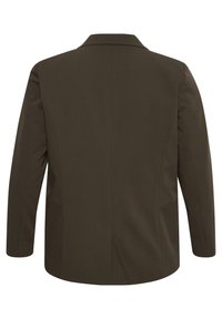 Blazer marron sur mesure avec un revers cranté, des épaules structurées et deux fentes au dos. Tissu lisse avec une finition mate. Manches longues.