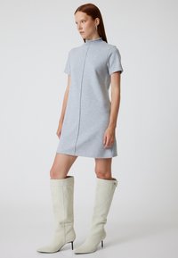 Grijs jurk met korte mouwen, hoge kraag en voornaad-detail, gecombineerd met kniehoog off-white stiletto laarzen. Gladde textuur.